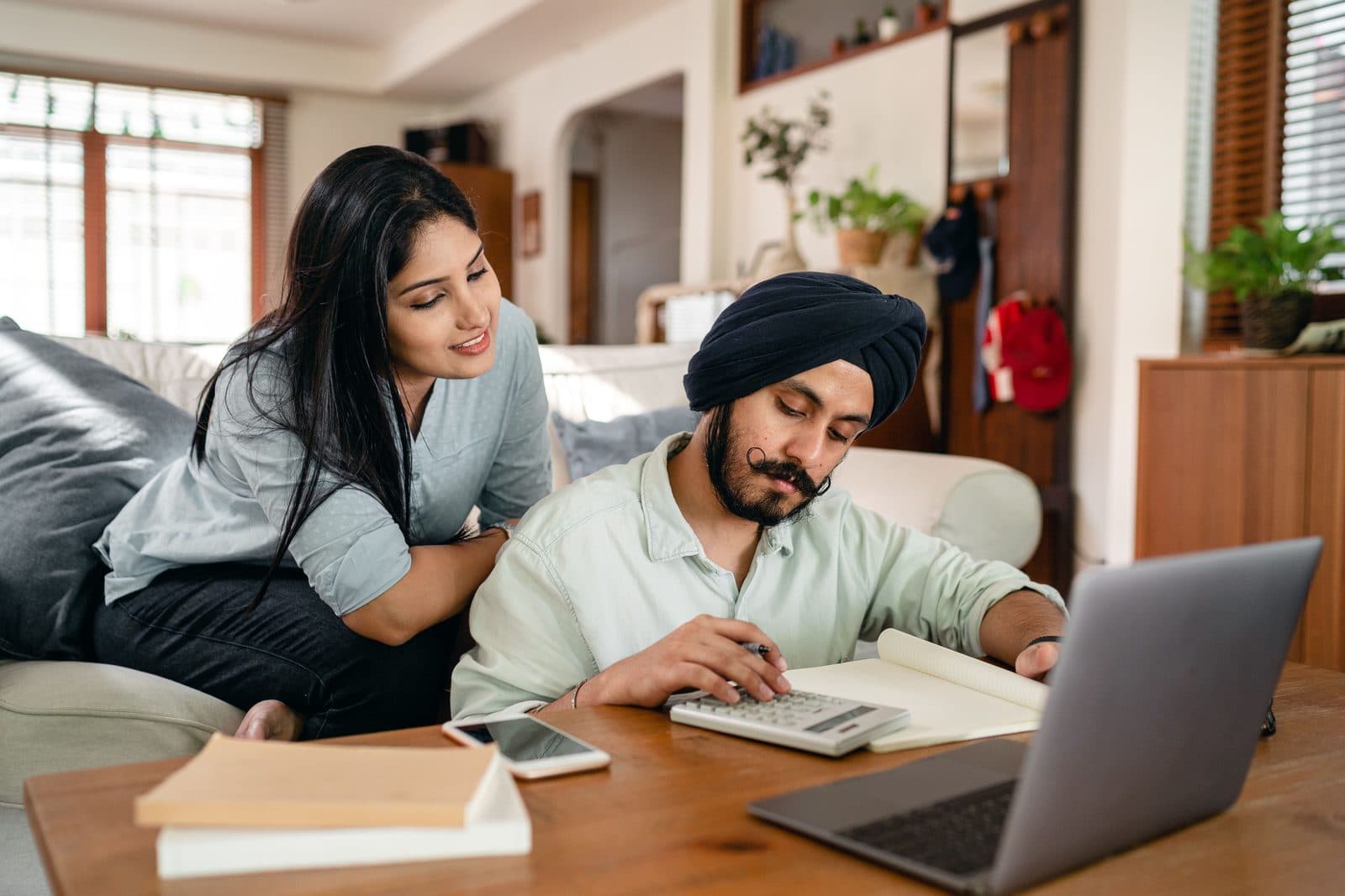 A man works through papers with a calculator at home while his wife looks on