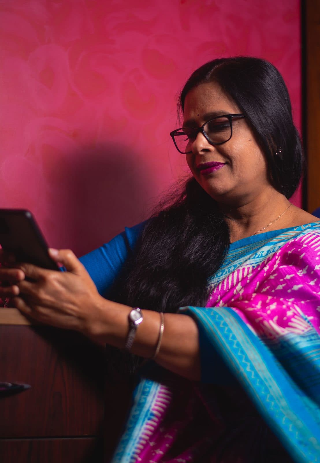 A woman in a saree checks her phone at home